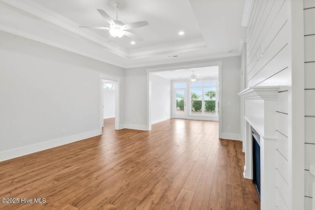 unfurnished living room featuring crown molding, ceiling fan, a raised ceiling, and light hardwood / wood-style flooring