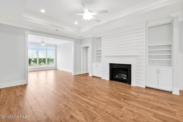 unfurnished living room with crown molding, light hardwood / wood-style flooring, a large fireplace, a raised ceiling, and built in features