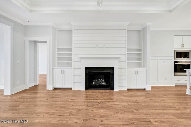 unfurnished living room with crown molding, built in shelves, and light wood-type flooring