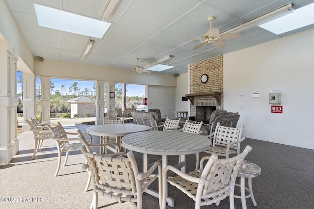 dining area with an outdoor brick fireplace, a drop ceiling, ceiling fan, and a skylight