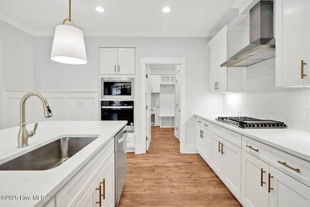 kitchen with pendant lighting, sink, appliances with stainless steel finishes, white cabinetry, and wall chimney exhaust hood