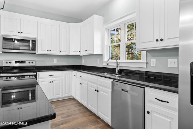 kitchen featuring appliances with stainless steel finishes, white cabinetry, dark stone countertops, wood-type flooring, and sink