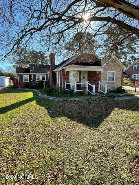 view of front of home with brick siding, a chimney, a front lawn, and a porch