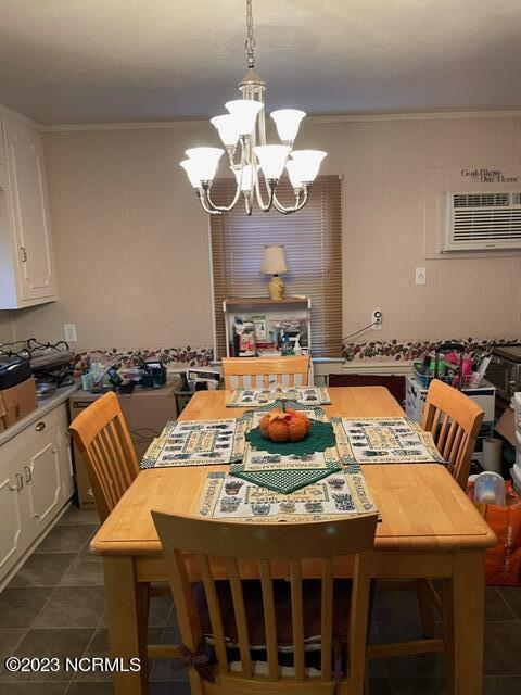 dining area with dark tile patterned floors, ornamental molding, a notable chandelier, and a wall mounted AC