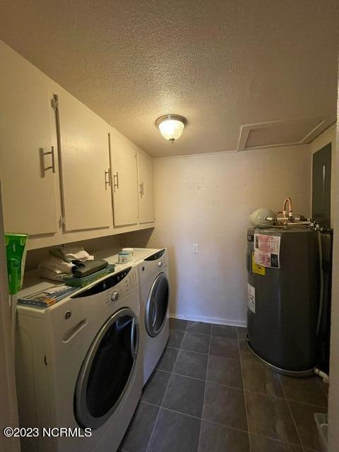 clothes washing area featuring a textured ceiling, electric water heater, separate washer and dryer, dark tile patterned floors, and cabinet space