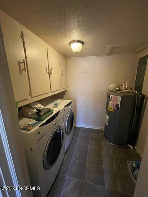 clothes washing area featuring dark tile patterned flooring, water heater, cabinet space, a textured ceiling, and washer and dryer