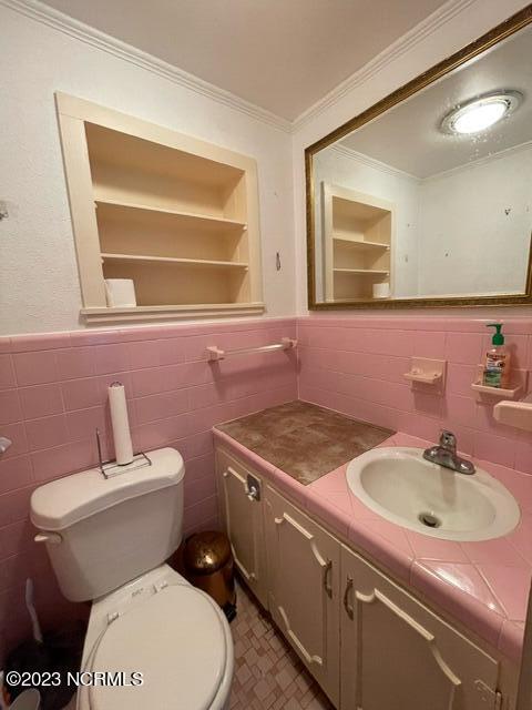 half bath featuring built in features, toilet, a wainscoted wall, ornamental molding, and vanity