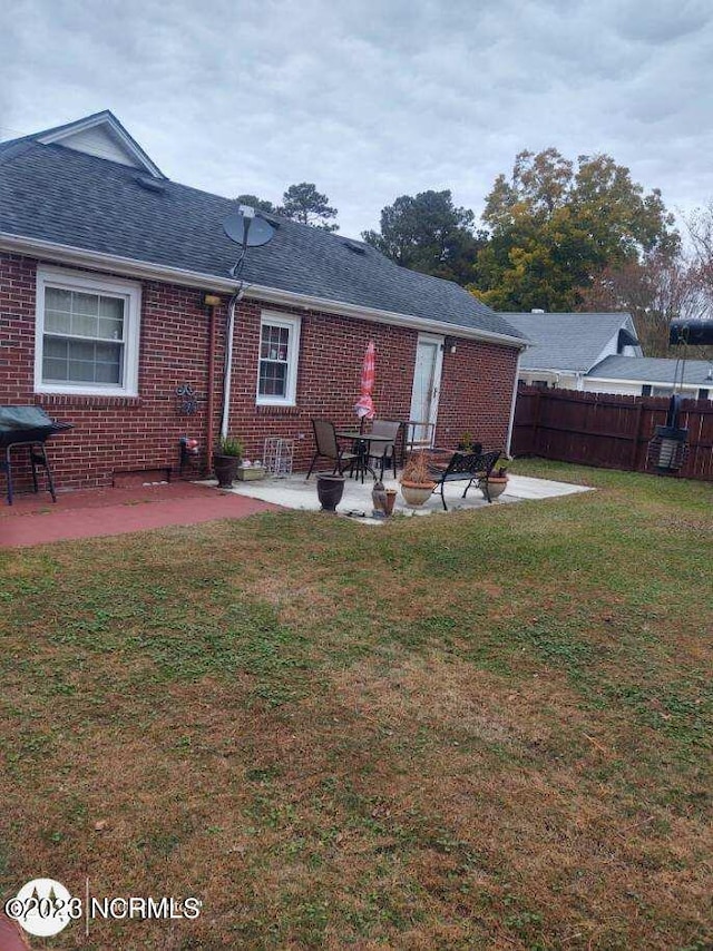 rear view of house with roof with shingles, a yard, brick siding, a patio, and fence