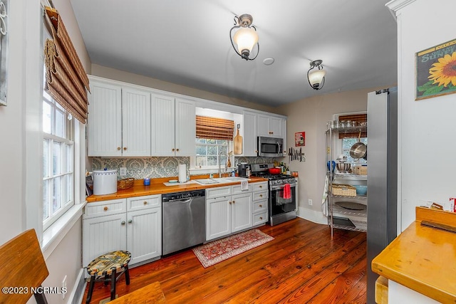 kitchen featuring sink, dark wood-type flooring, tasteful backsplash, white cabinets, and appliances with stainless steel finishes