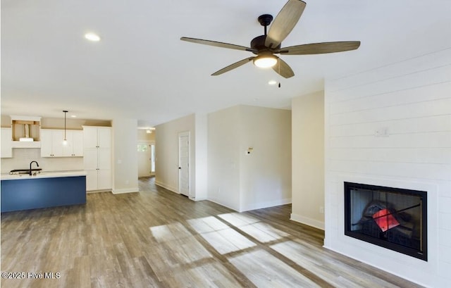 unfurnished living room with recessed lighting, a large fireplace, a sink, baseboards, and light wood-type flooring