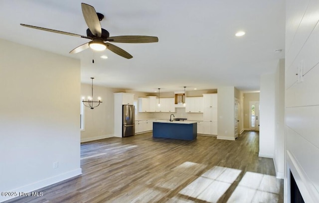 kitchen with freestanding refrigerator, light countertops, an island with sink, and wood finished floors