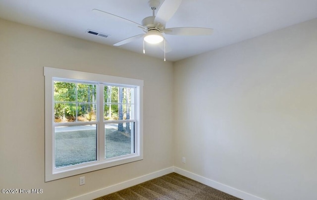 spare room featuring a ceiling fan, visible vents, dark carpet, and baseboards