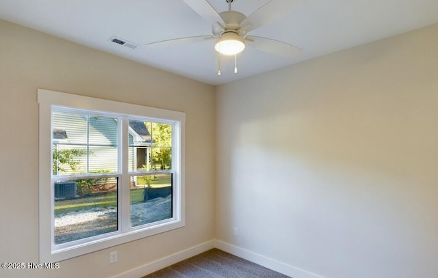 unfurnished room with baseboards, visible vents, dark carpet, and a ceiling fan