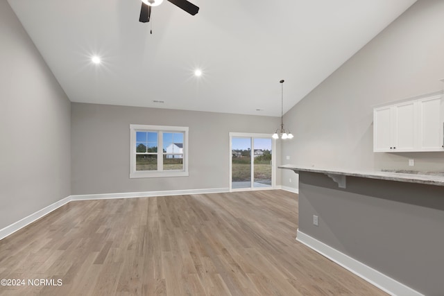 unfurnished living room with high vaulted ceiling, light hardwood / wood-style floors, and ceiling fan with notable chandelier