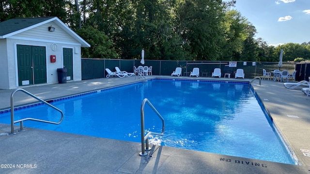 pool with a patio area, fence, and an outdoor structure