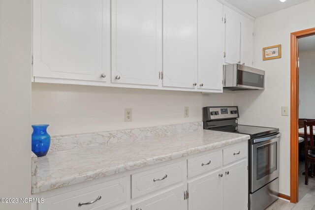 kitchen with appliances with stainless steel finishes, light hardwood / wood-style floors, light stone countertops, and white cabinetry