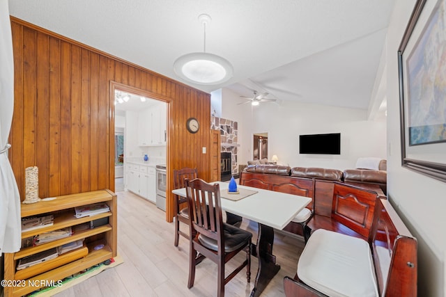 dining space with a stone fireplace, lofted ceiling, light wood-type flooring, and ceiling fan