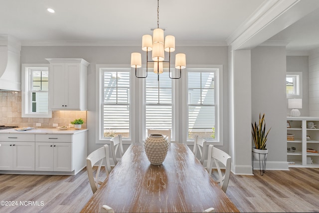 dining room with light wood-type flooring, ornamental molding, a notable chandelier, and a healthy amount of sunlight