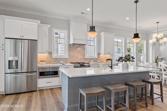 kitchen with custom range hood, appliances with stainless steel finishes, light hardwood / wood-style floors, white cabinetry, and an island with sink