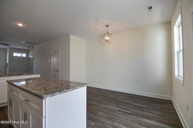 kitchen featuring pendant lighting, dark wood-type flooring, white cabinetry, dark stone countertops, and a center island