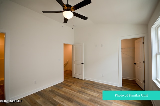 unfurnished bedroom with a walk in closet, vaulted ceiling, ceiling fan, light wood-type flooring, and a closet