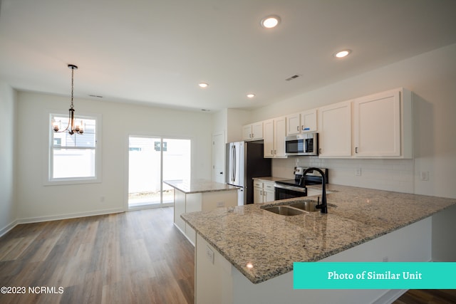 kitchen with kitchen peninsula, light stone countertops, stainless steel appliances, white cabinetry, and hanging light fixtures