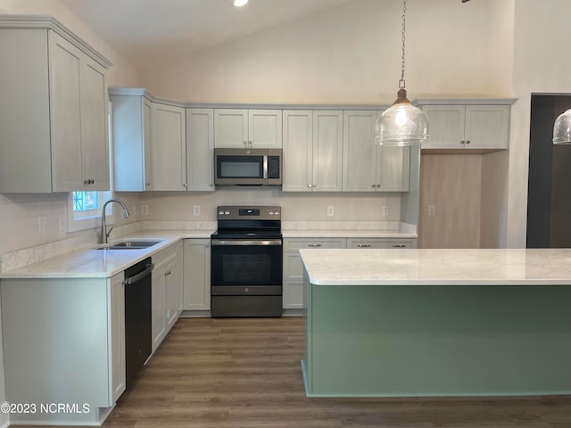 kitchen featuring light stone counters, hardwood / wood-style floors, appliances with stainless steel finishes, sink, and pendant lighting