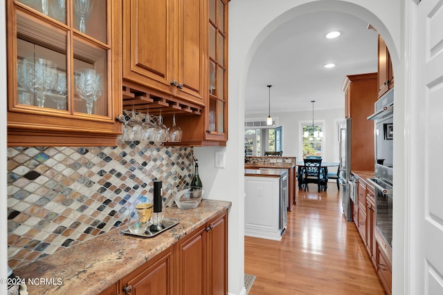 kitchen with decorative light fixtures, light hardwood / wood-style flooring, tasteful backsplash, oven, and light stone counters