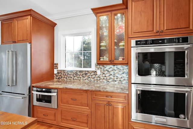 kitchen with light stone countertops, appliances with stainless steel finishes, light hardwood / wood-style flooring, backsplash, and ornamental molding