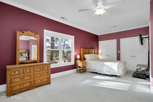 carpeted bedroom featuring ornamental molding, ceiling fan, and multiple closets