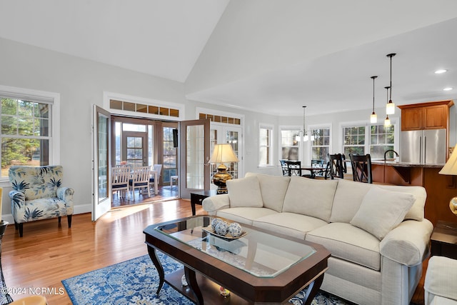 living room featuring high vaulted ceiling, a notable chandelier, sink, light wood-type flooring, and french doors