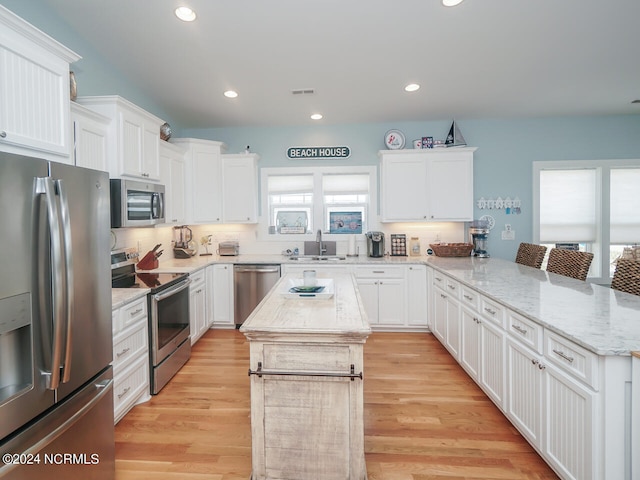 kitchen with appliances with stainless steel finishes, white cabinetry, a sink, a kitchen island, and a peninsula