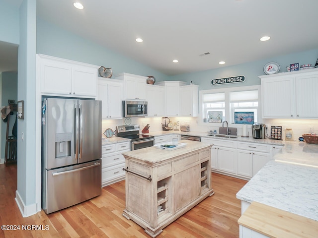 kitchen with decorative backsplash, appliances with stainless steel finishes, a center island, light wood-style floors, and a sink