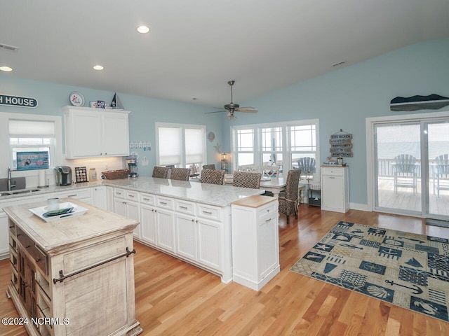 kitchen with a healthy amount of sunlight, vaulted ceiling, a peninsula, and light wood finished floors