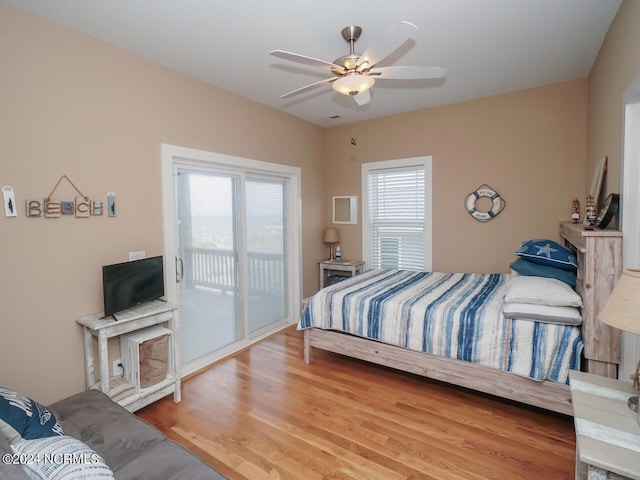 bedroom with access to outside, multiple windows, wood finished floors, and a ceiling fan