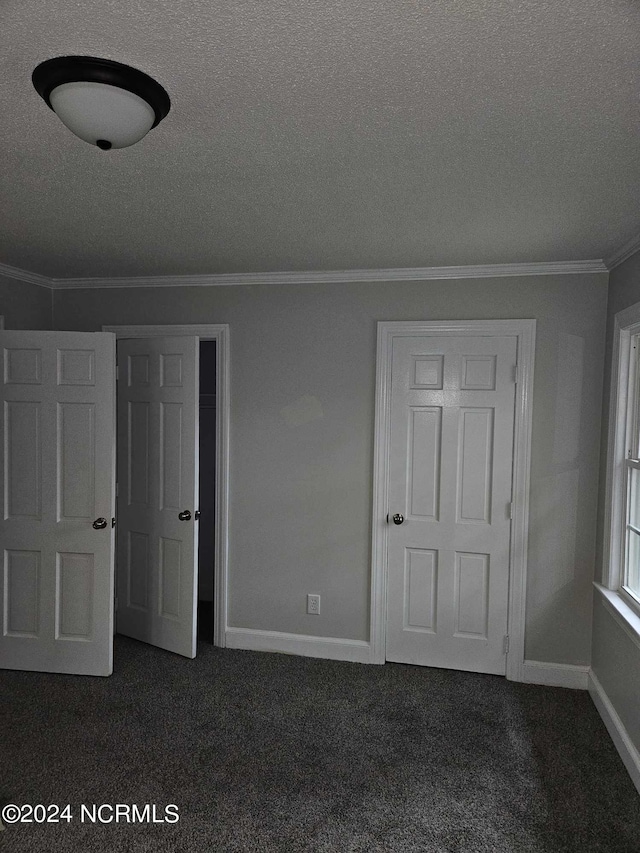 unfurnished bedroom featuring a textured ceiling, dark carpet, and ornamental molding