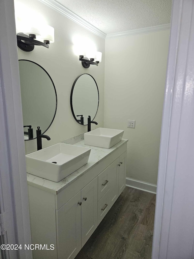 bathroom with hardwood / wood-style flooring, a textured ceiling, crown molding, and dual bowl vanity