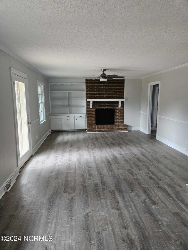 unfurnished living room featuring a textured ceiling, ceiling fan, a brick fireplace, hardwood / wood-style flooring, and ornamental molding