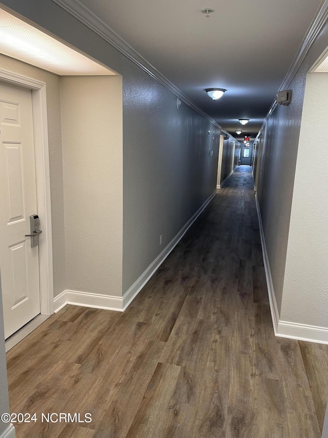 corridor with dark wood finished floors, ornamental molding, and baseboards