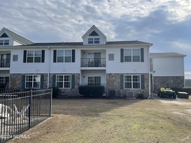 rear view of house featuring stone siding, central air condition unit, and a balcony
