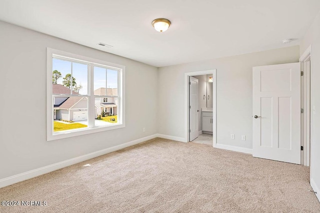 unfurnished bedroom featuring light carpet and ensuite bathroom