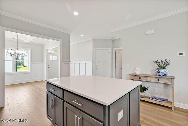 kitchen featuring pendant lighting, a center island, ornamental molding, a notable chandelier, and light wood-type flooring