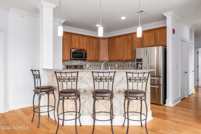 kitchen featuring crown molding, pendant lighting, tasteful backsplash, a kitchen bar, and stainless steel appliances