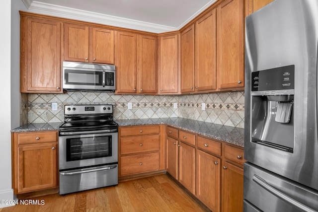 kitchen with crown molding, appliances with stainless steel finishes, decorative backsplash, light hardwood / wood-style flooring, and dark stone counters