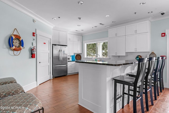 kitchen featuring crown molding, stainless steel refrigerator, decorative backsplash, white cabinets, and dark stone counters