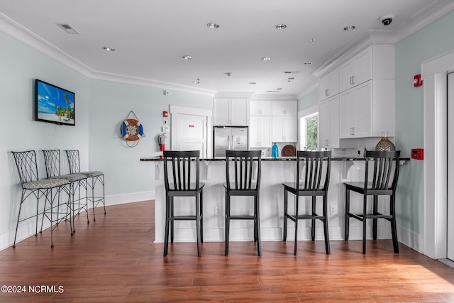 kitchen featuring stainless steel fridge, dark wood-type flooring, white cabinetry, ornamental molding, and a breakfast bar area