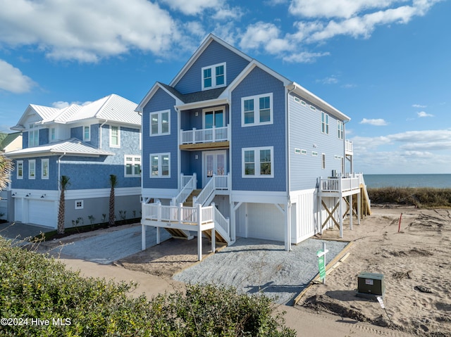 rear view of house featuring an attached garage, a balcony, a water view, stairway, and gravel driveway