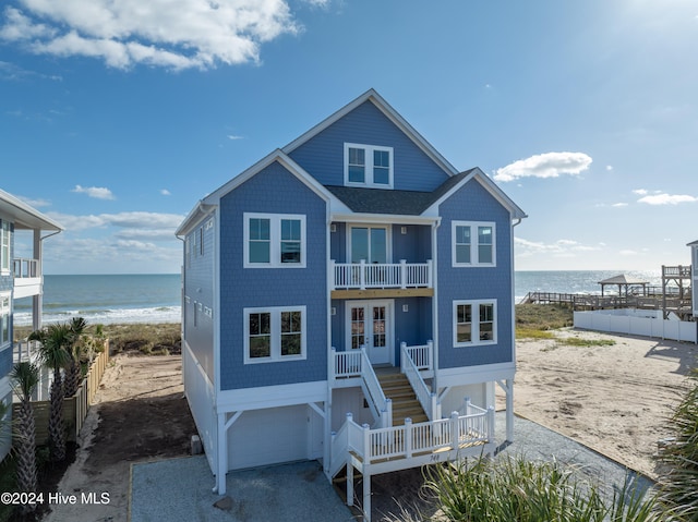 coastal home with an attached garage, a view of the beach, a water view, stairs, and french doors