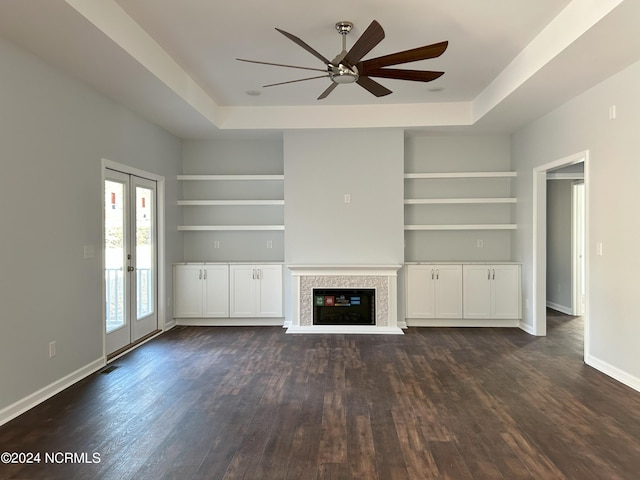 unfurnished living room featuring built in shelves, ceiling fan, a raised ceiling, and french doors