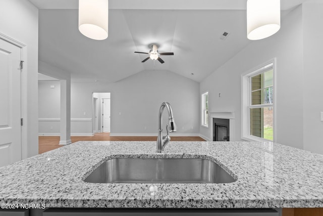 kitchen featuring ceiling fan, hardwood / wood-style floors, sink, light stone counters, and vaulted ceiling